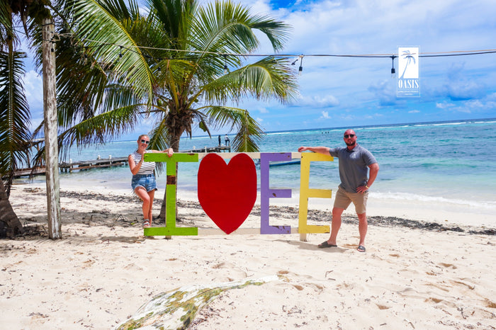 Two people by the I love EE sign on the beach at East End, Grand Cayman