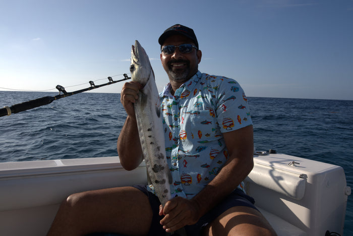 A man on a boat holding a fish he has caught off Cayman Brac